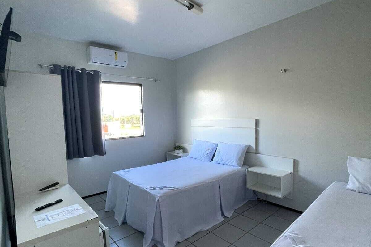 A hotel room with two single beds, a desk, a chair, a small table, and a window with curtains.