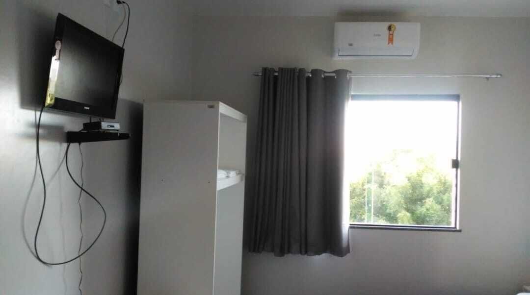 A room with a television on a stand, a window with curtains, and an air conditioning unit on the wall.