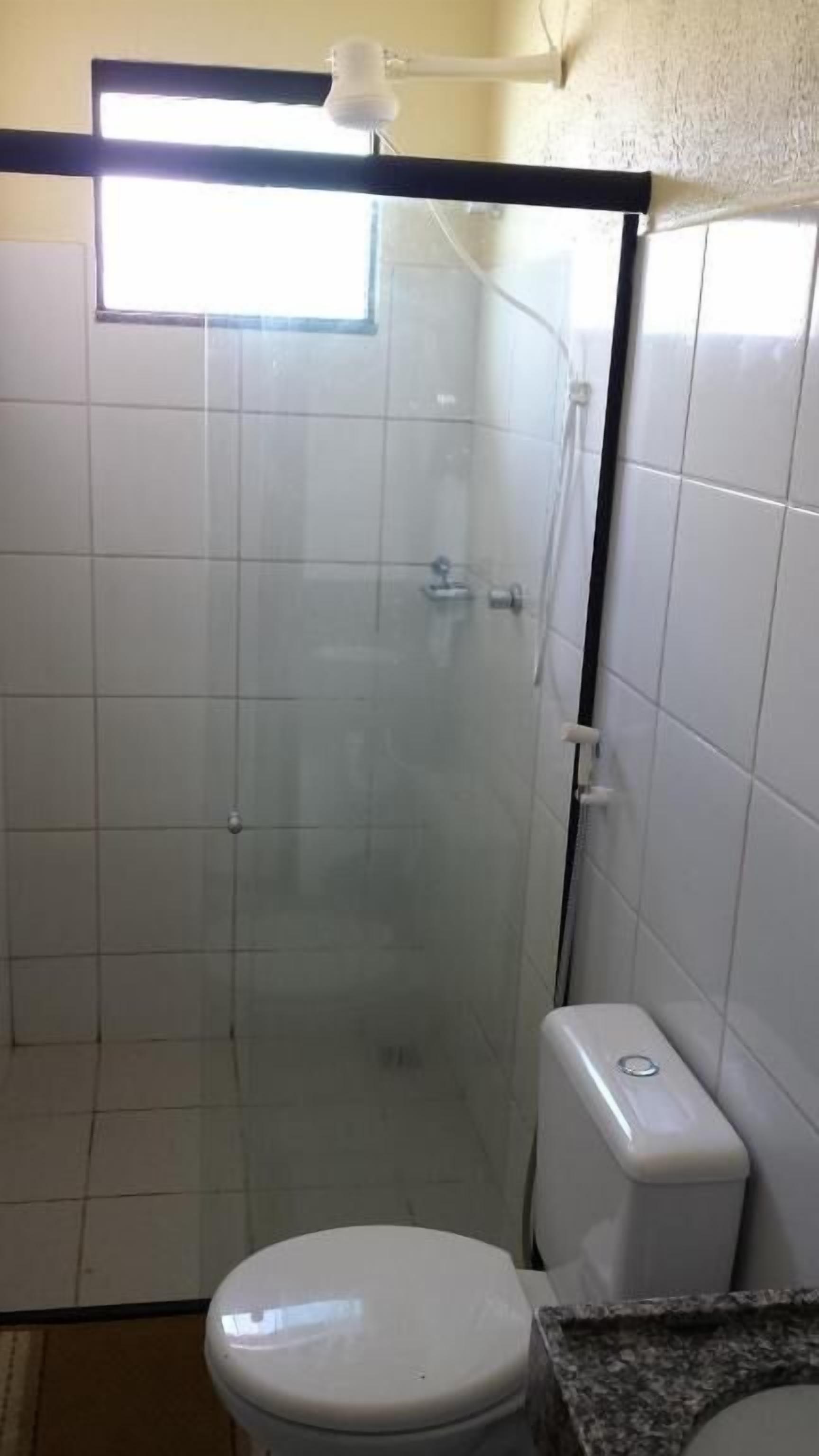 Une petite salle de bain fermée, comprenant des toilettes, un espace douche et une fenêtre.