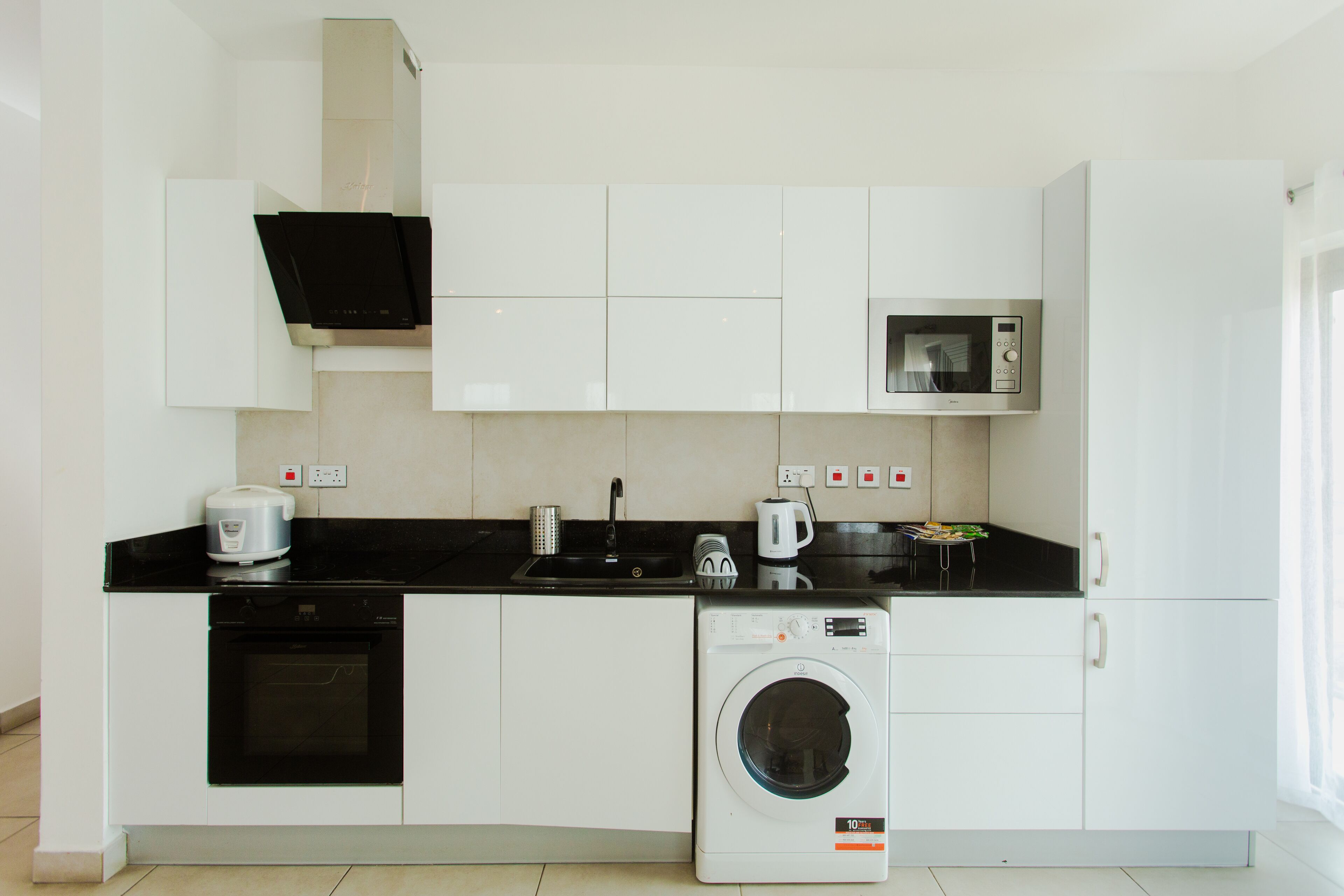 A compact kitchen with a washing machine, microwave, oven, and a coffee maker.
