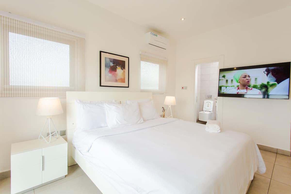Une chambre d’hôtel avec un grand lit, deux tables de chevet avec des lampes, une télévision et un appareil de climatisation.