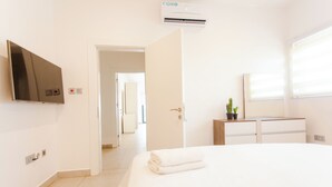 Hotelkamer met een bed, een aan de muur bevestigde televisie, een kamerplant en een raam met jaloezieën.