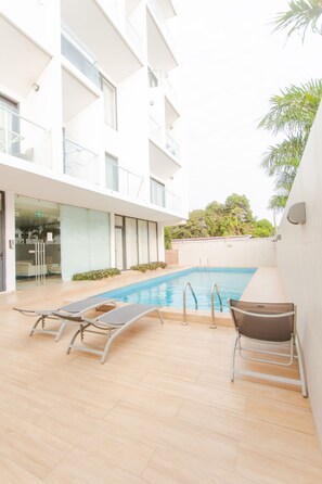 A modern building with a swimming pool, lounge chairs, and a small table.