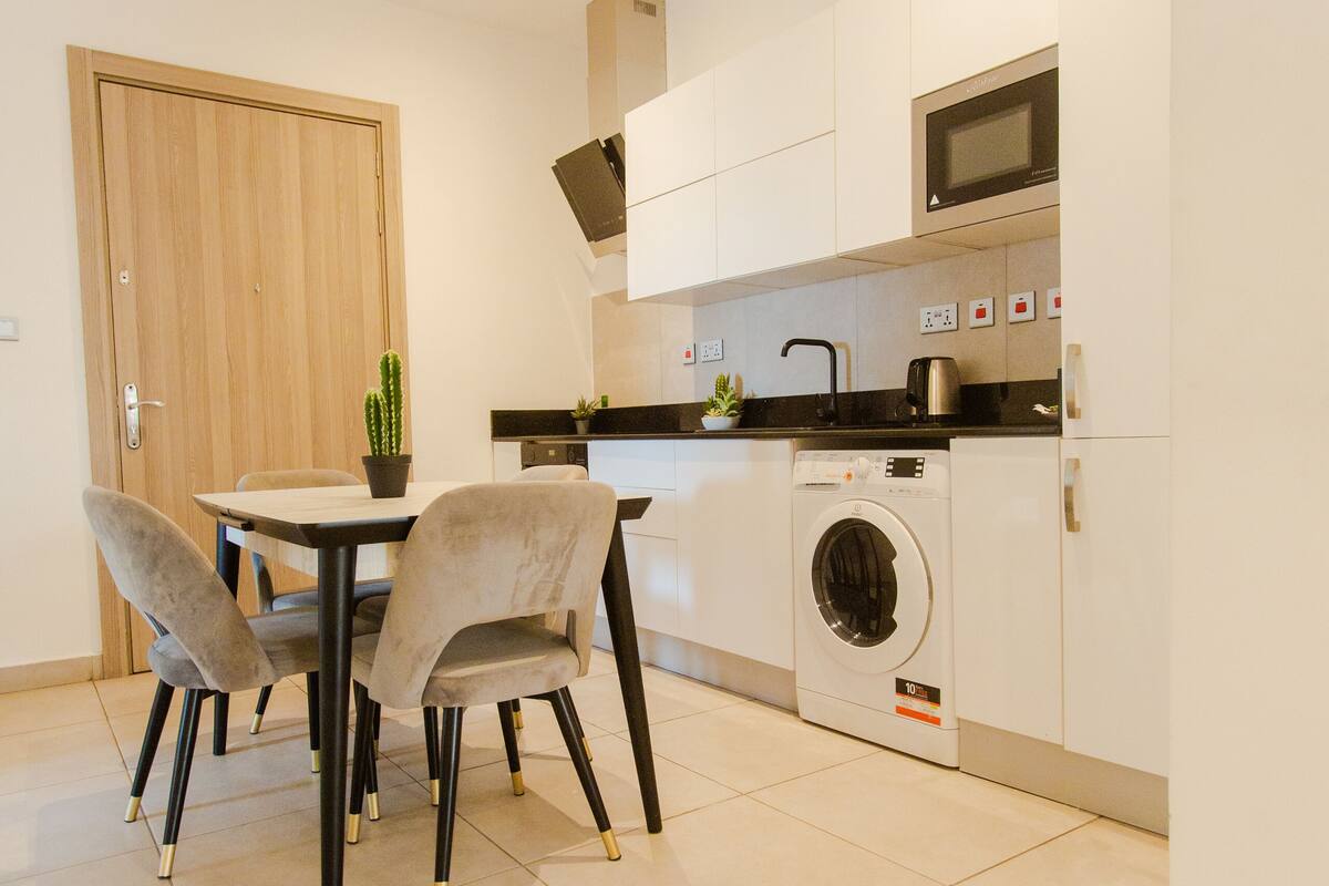 Une cuisine compacte comprenant une table à manger, des chaises, un lave-linge et un four à micro-ondes.