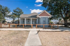 A two-story house with a front porch, a fenced yard, and a clear sky. - AAV Home Unit A-New!Adorable 2BR Near Fort Sam/Pearl/DT (San Antonio)