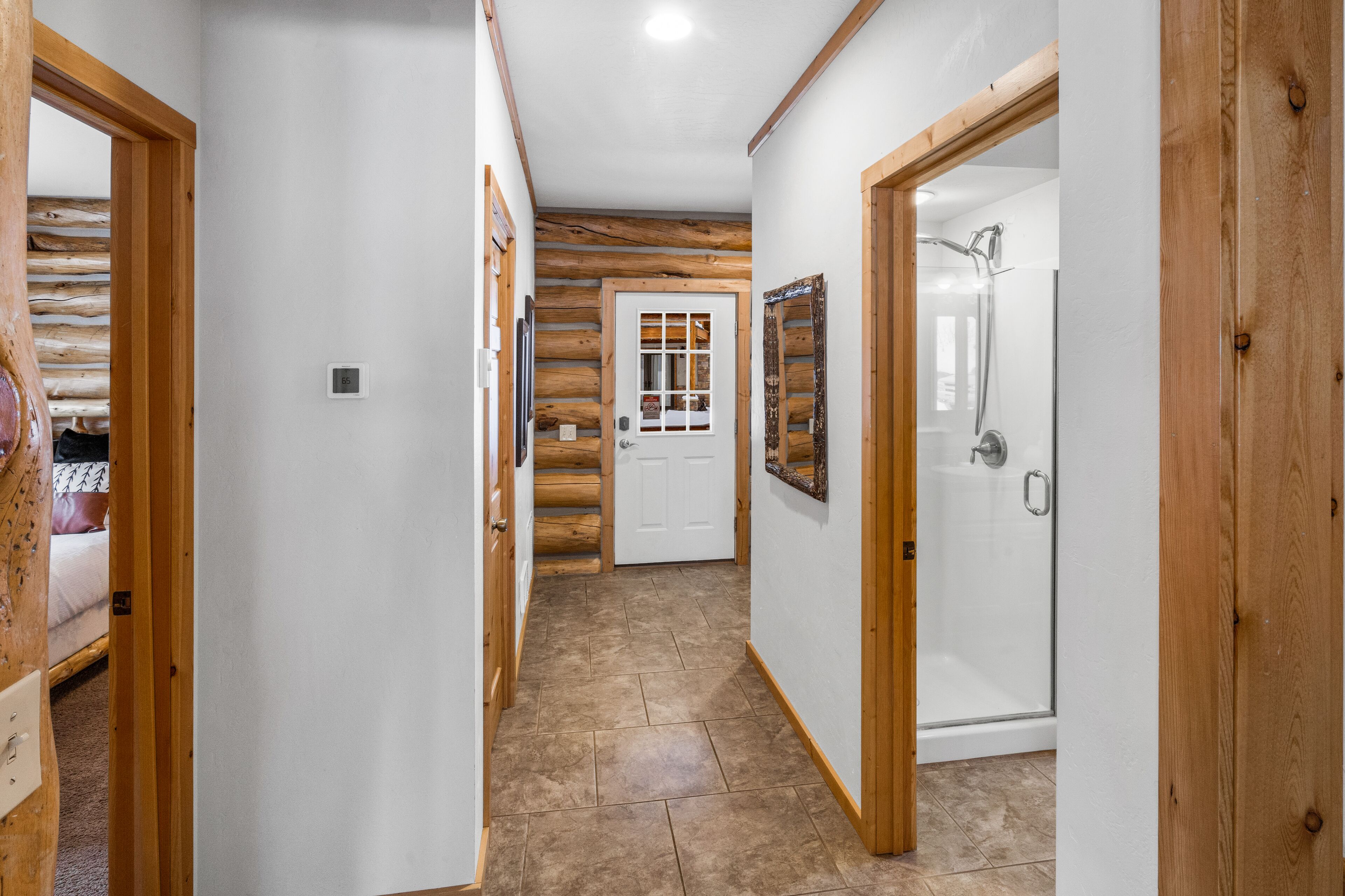 Un pasillo con paredes de madera y suelo de baldosas, que conduce a un dormitorio con cama y un baño con ducha.