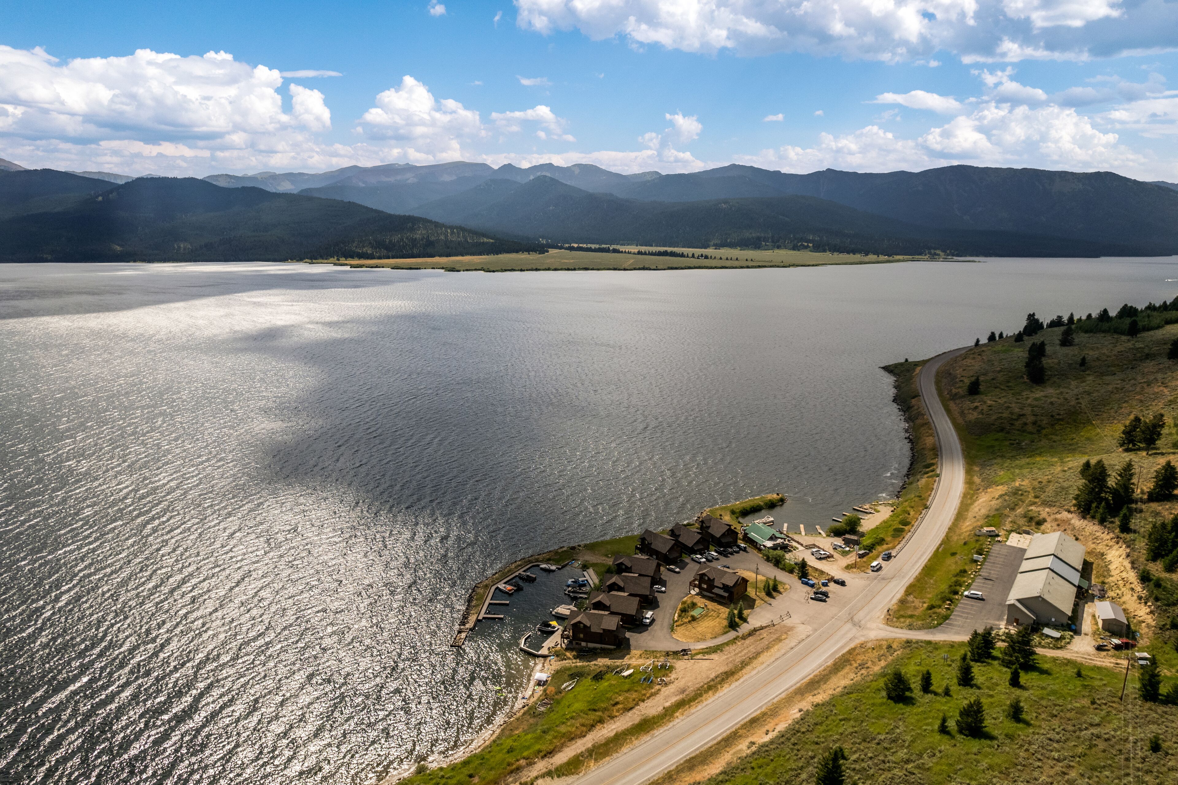An aerial view of a lakeside property with a marina, several buildings, and a road leading to the water.