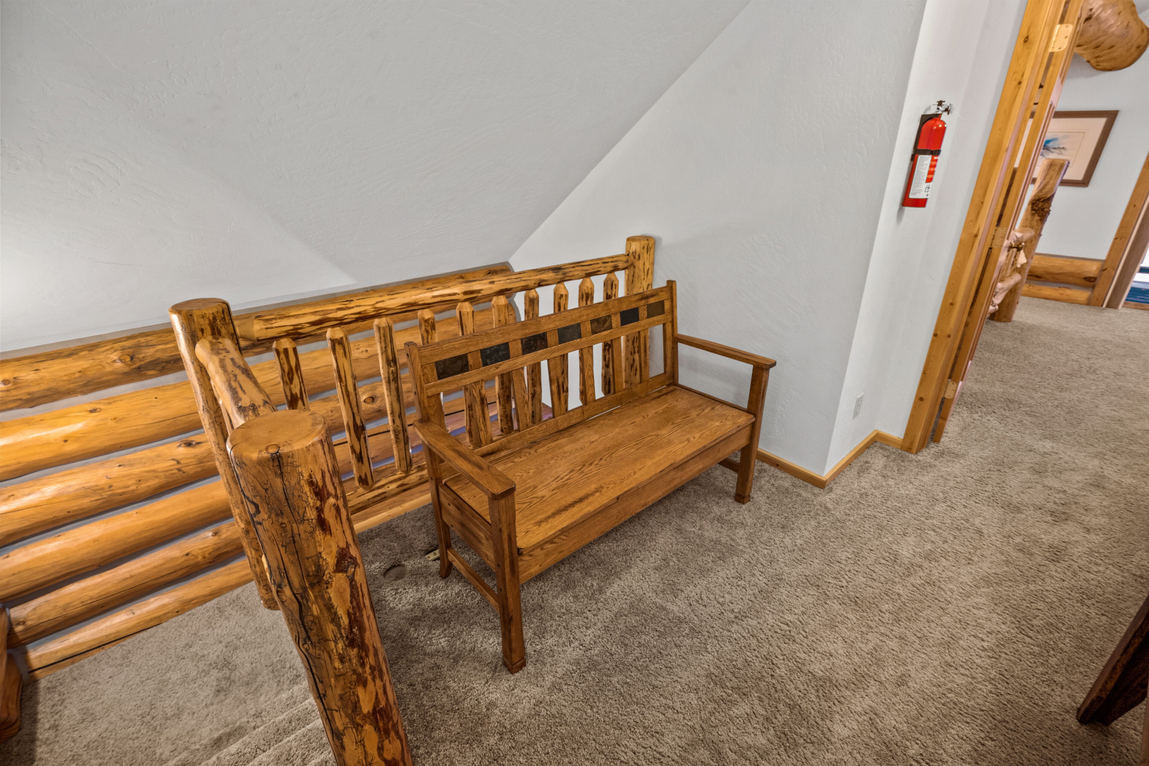 Un banco de madera en una habitación con techo inclinado y un extintor en la pared.
