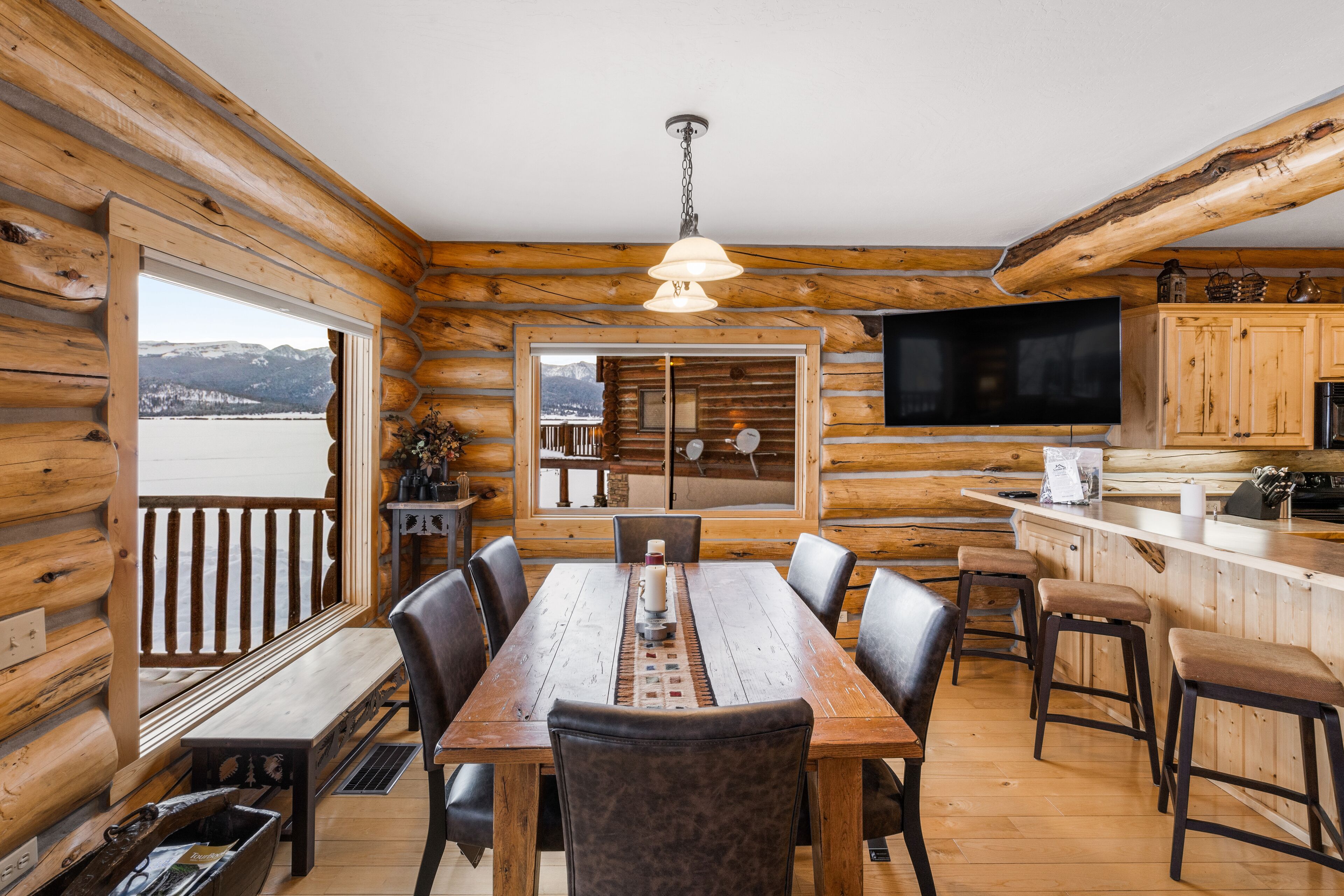 Una cabaña de madera con comedor, cocina y un amplio ventanal con vista a un lago.