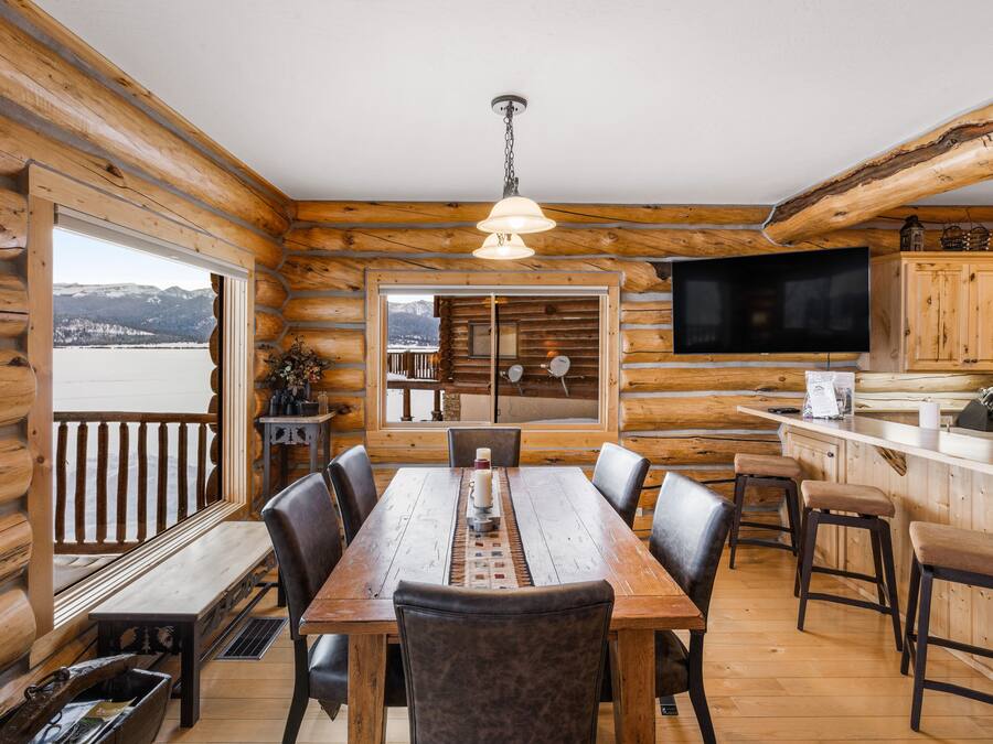 Una cabaña de madera con comedor, cocina y un amplio ventanal con vista a un lago.