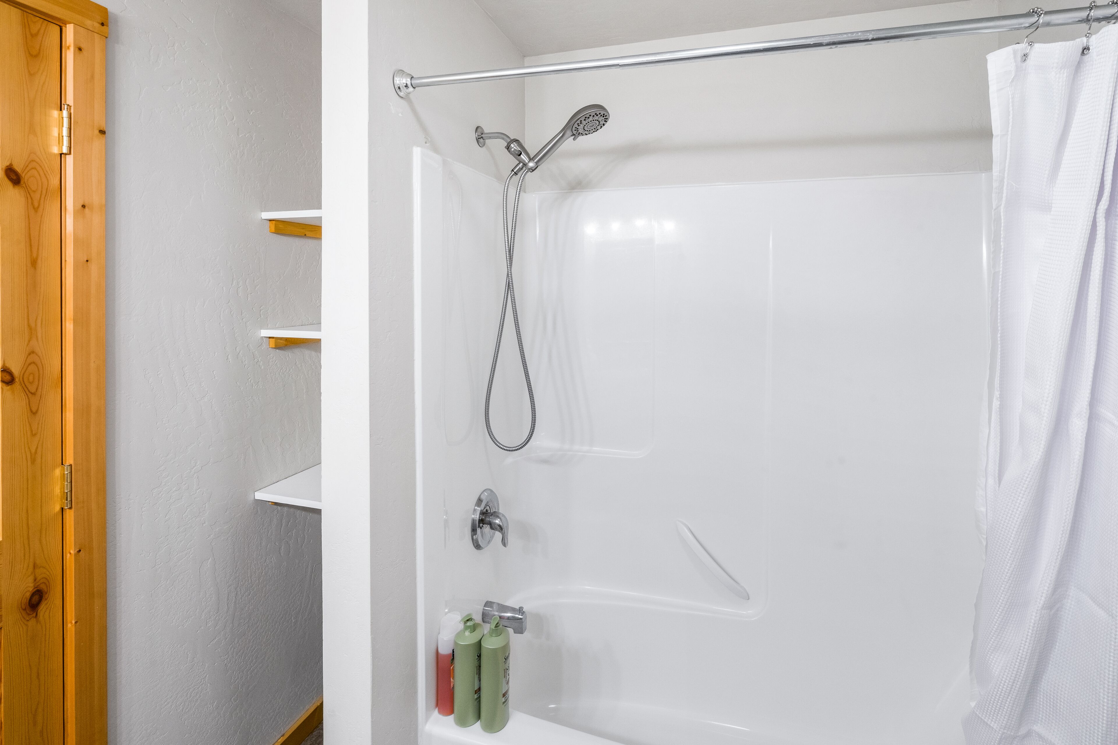A white bathtub with a showerhead, a towel rack, and a wooden door.