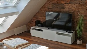 Quarto moderno no estilo loft, com teto inclinado, parede de tijolos, uma grande TV de tela plana sobre um móvel branco e um domo de vidro.