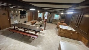 Amplia sala de estar con una gran mesa de madera, un sofá y una chimenea. Se observa una cocina con armarios de madera y una encimera.
