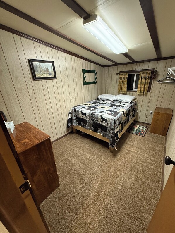 A bedroom with a bed, wooden walls, a window with curtains, a desk, and a carpeted floor. - Private family lodge on 42 serene acres- 15 minutes to Penn State- Centre County (Howard)