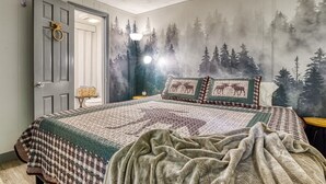 Ein Schlafzimmer mit einem großen Bett, einem Wandbild mit Waldmotiv und einer Tür mit Messingklinke.