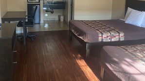 Quarto de hotel com piso de madeira, cama com colcha estampada, escrivaninha com micro-ondas, uma cadeira e uma pequena lixeira.