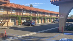 Um motel com telhado de telhas vermelhas, estacionamento com vagas para deficientes e uma placa de 'Proibido Estacionar'.