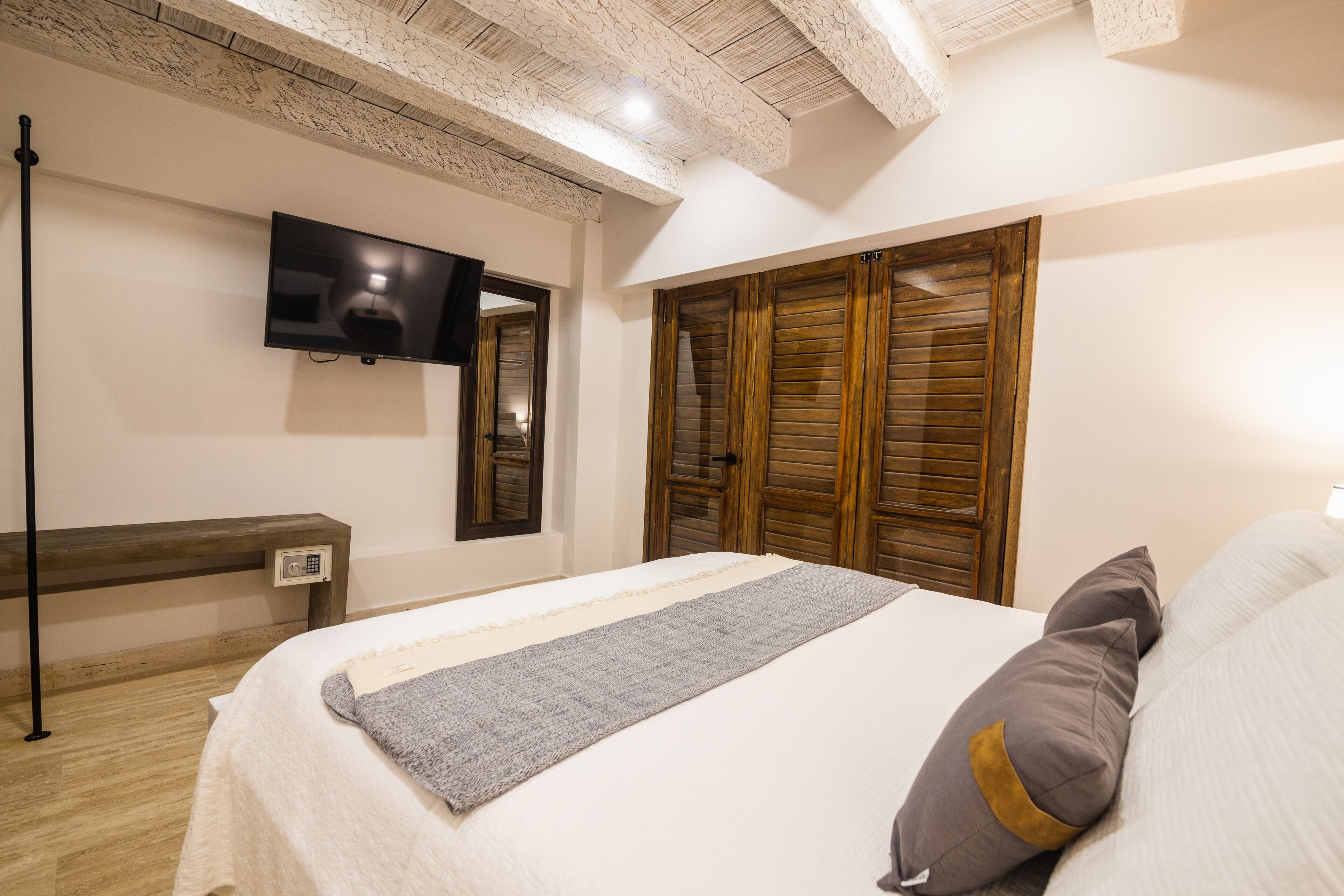 A bedroom with a bed, a television mounted on the wall, wooden wardrobes, and a bench.