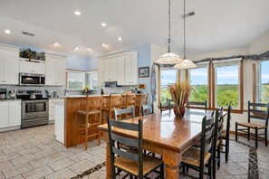 A spacious kitchen with white cabinets, a wooden island, and a large dining table with chairs. - Pet-Friendly Beach Escape with Elevator, Pool Cabana Bar w/TV & Scenic Deck View (Corolla)