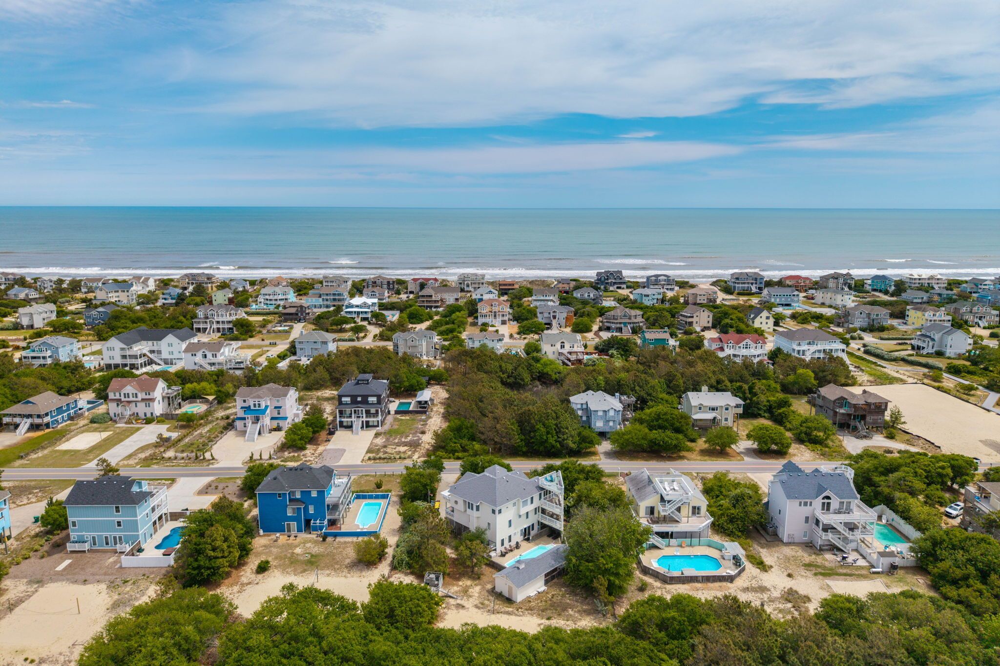 Vue aérienne d’une zone résidentielle côtière, avec des maisons, une plage et un ciel dégagé.