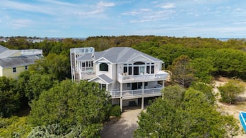 Une grande maison à deux étages, dotée d’un balcon, entourée d’une végétation luxuriante et offrant une vue dégagée sur l’océan.