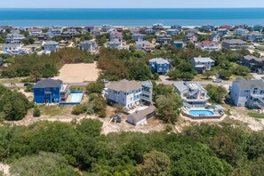 An aerial view of a coastal residential area with houses, a beach, and a large swimming pool. - Pet-Friendly Beach Escape with Elevator, Pool Cabana Bar w/TV & Scenic Deck View (Corolla)