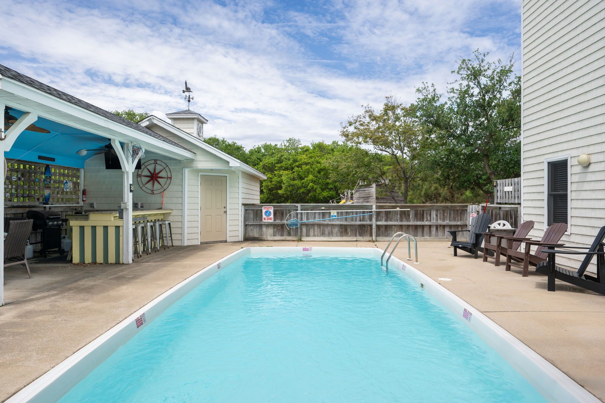 A swimming pool with a deck area, a covered bar, and a fenced-in section with lounge chairs.
