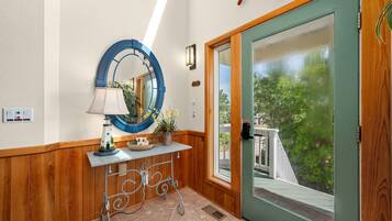 Un intérieur en bois avec une porte verte, un miroir rond, une petite table avec une lampe et une plante en pot.