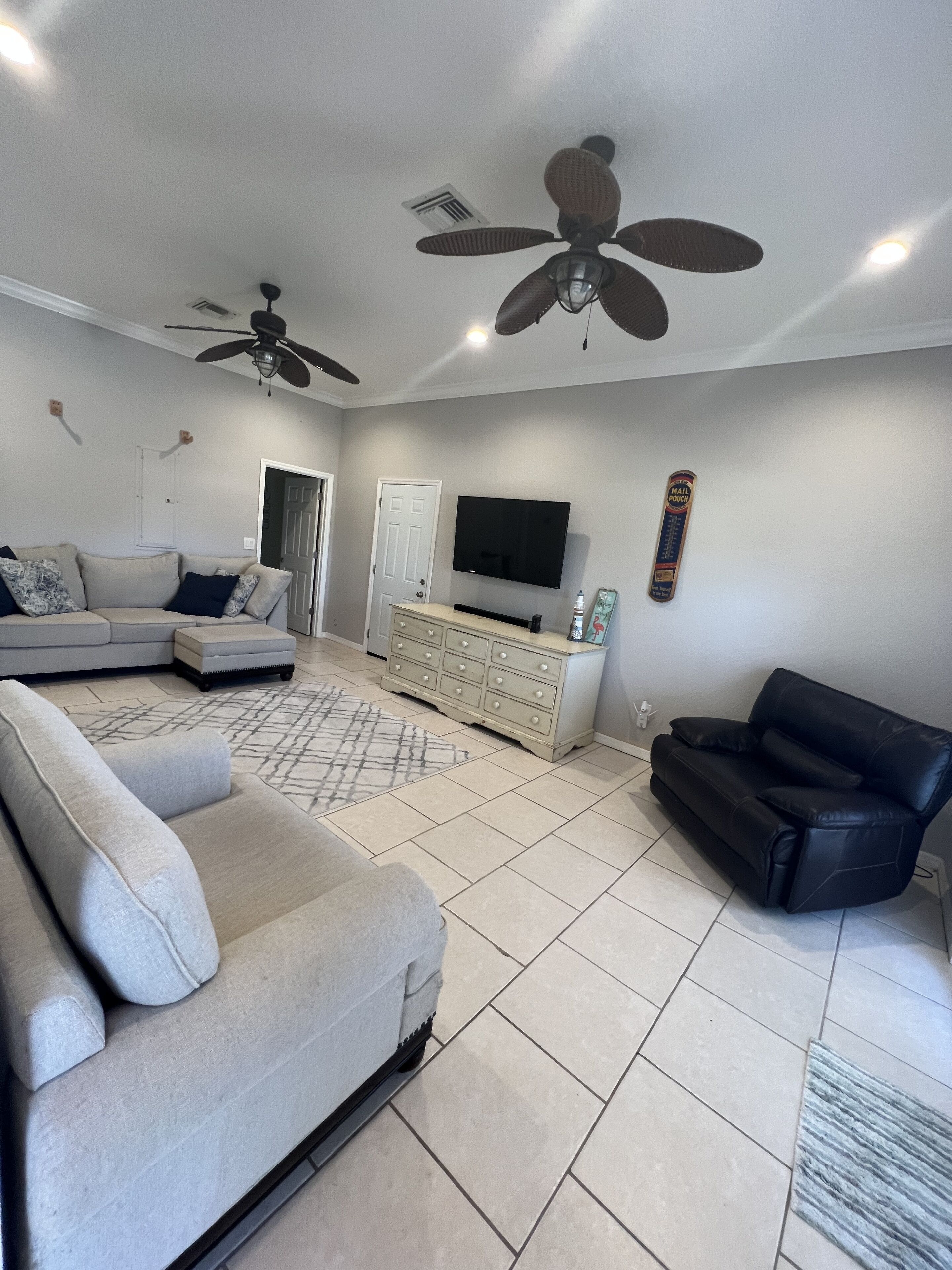 A living room with a grey sofa, a black leather couch, a TV, and a ceiling fan.