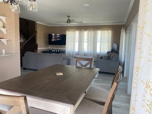 Un salon avec une table à manger en bois, des canapés gris, un téléviseur et un ventilateur de plafond.