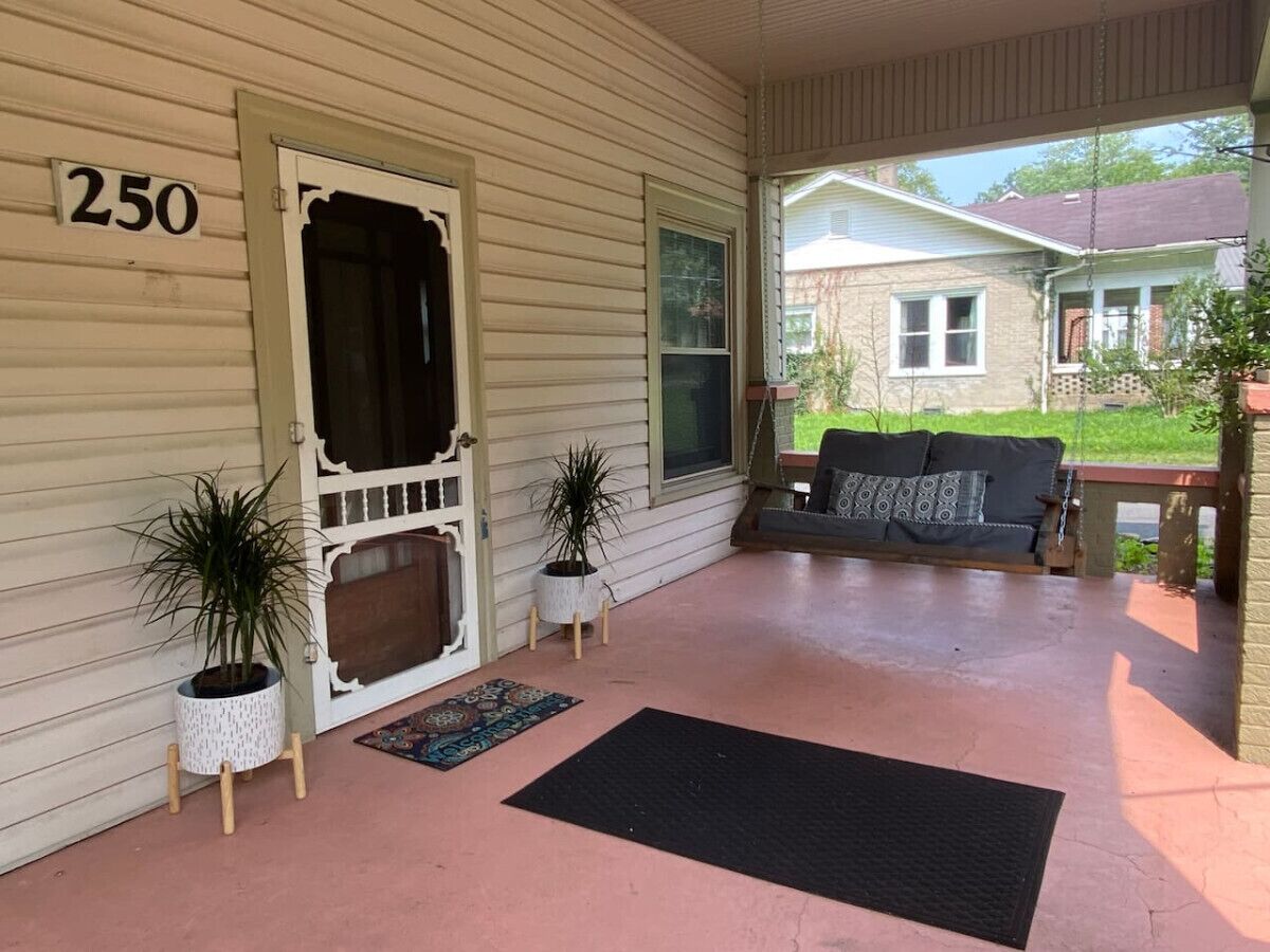 A covered porch with a number '250' on the wall, two potted plants, a black doormat, and a sofa with cushions.