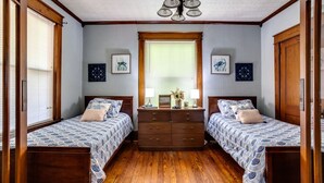 A bedroom with two beds, wooden floors, a dresser, and a ceiling fan.
