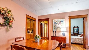A dining area with a wooden table and chairs, a vase with flowers, and a painting on the wall.