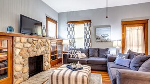 A living room with a stone fireplace, a grey sofa, and a television mounted on the wall.