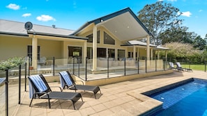 Une maison moderne dotée d’une piscine, d’un espace salon extérieur et d’une terrasse clôturée.