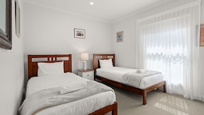 Une chambre d’hôtel avec deux lits simples, une table de chevet avec une lampe et une grande fenêtre avec des rideaux légers.