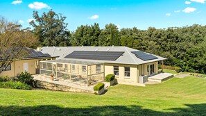 Une maison moderne dotée de panneaux solaires sur le toit, d’une serre en verre et d’une pelouse bien entretenue.