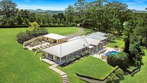 Una casa de dos pisos con un amplio jardín delantero, una piscina y un jardín muy cuidado.