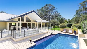 Una casa moderna con una piscina grande, mobiliario de exterior y un jardín bien cuidado.