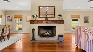 Una sala de estar con chimenea, un espejo grande encima y vistas al exterior a través de las ventanas.
