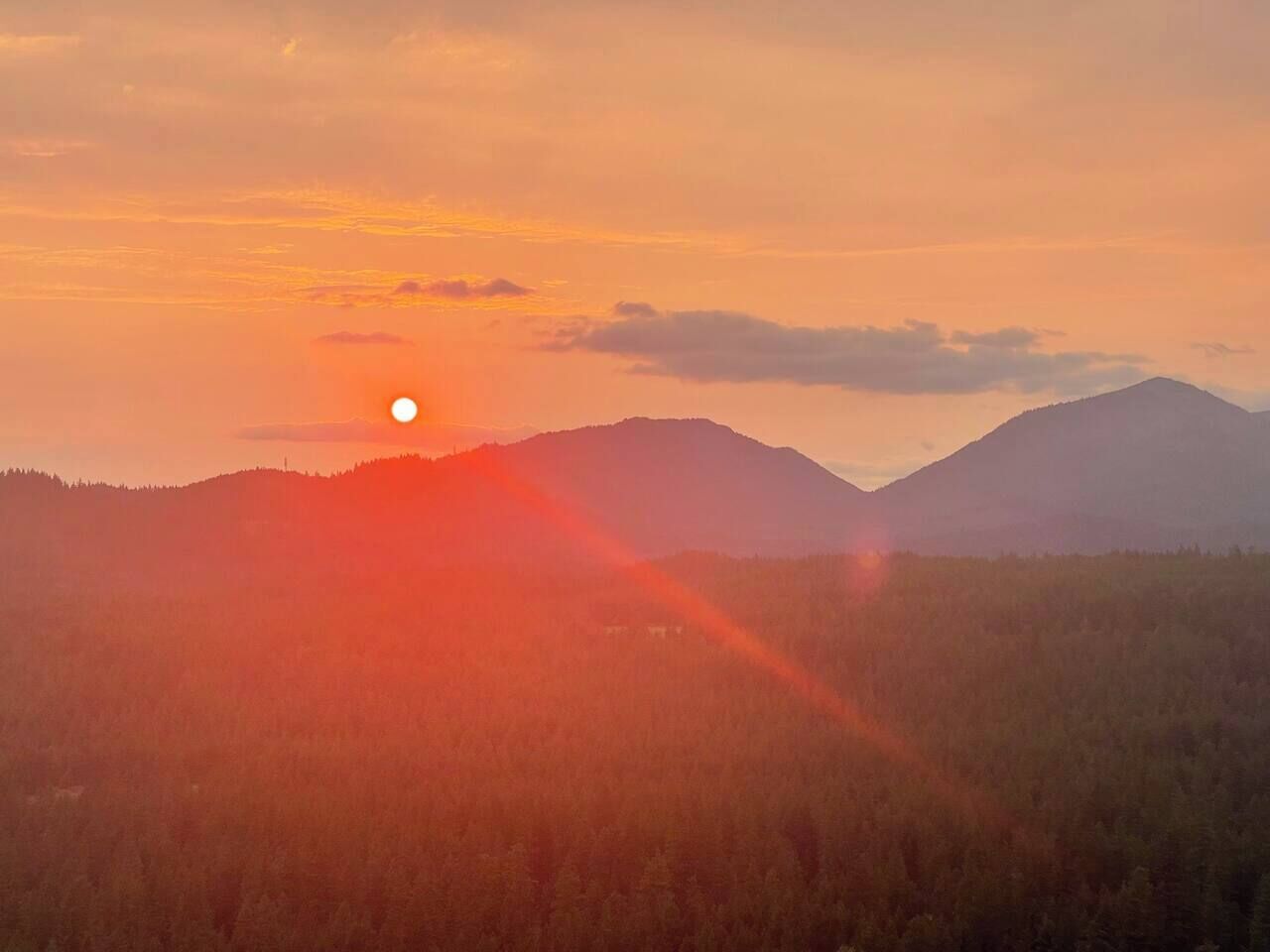 A sunset over a mountainous landscape with a forested area in the foreground.