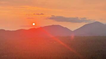 A sunset over a mountainous landscape with a forested area in the foreground.