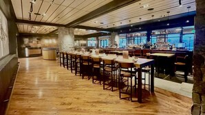 Ein Restaurant mit einem langen Holztisch und Stühlen, einer Bar mit Regalen voller Flaschen und einer Steinwand.