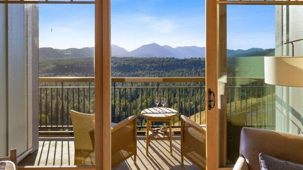 Ein Balkon mit Korbmöbeln und einem Tisch, der Blick ins bewaldete Tal und auf die Berge gewährt.
