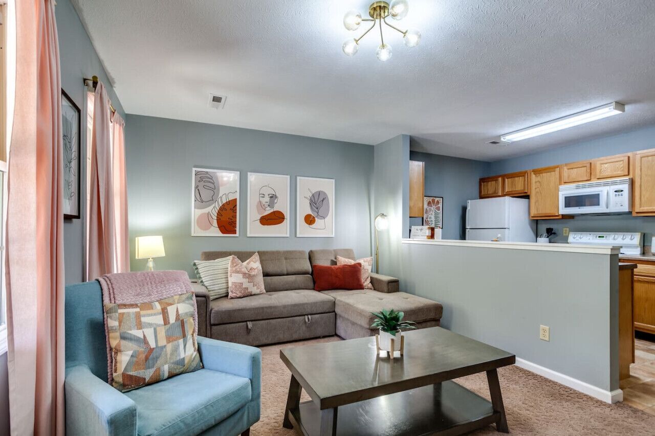 A living room with a sectional sofa, a coffee table, and a kitchen area with wooden cabinets and a microwave.