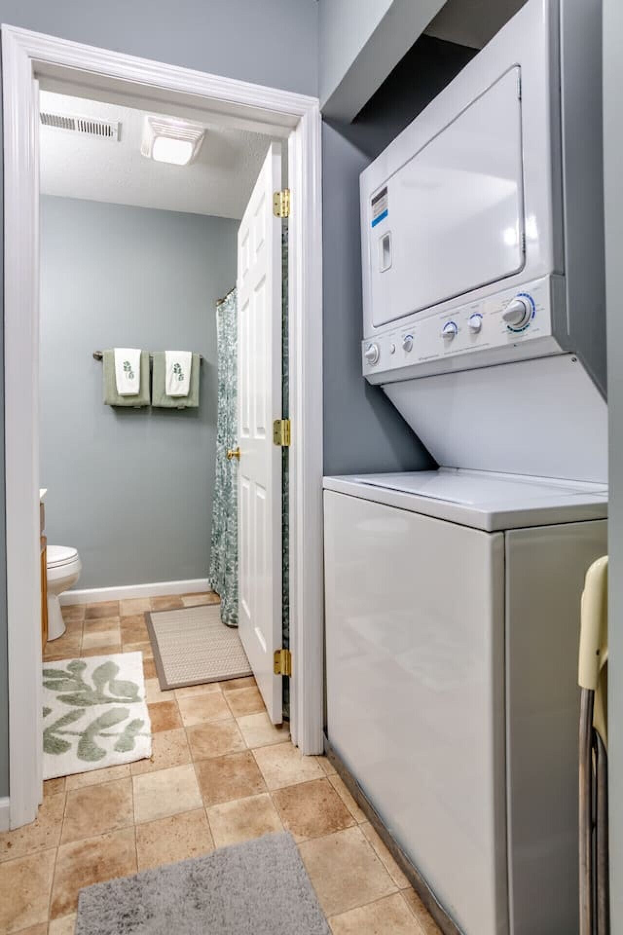 A laundry room with a washing machine and dryer, a door leading to a bathroom, and a patterned rug on the floor.