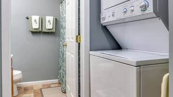 A laundry room with a washing machine and dryer, a door leading to a bathroom, and a patterned rug on the floor.