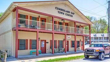 Um edifício de dois andares com varanda, mesas ao ar livre e um veículo estacionado, identificado com a placa 'Cumberland Gap Town Center'.