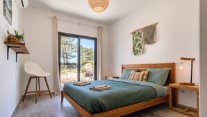 Una camera da letto con un letto in legno, una sedia bianca, un tavolino e vista sull'esterno.