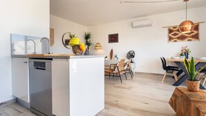 Una cucina funzionale con lavastoviglie, zona pranzo con tavolo e sedie in legno, e un'isola con una pianta.